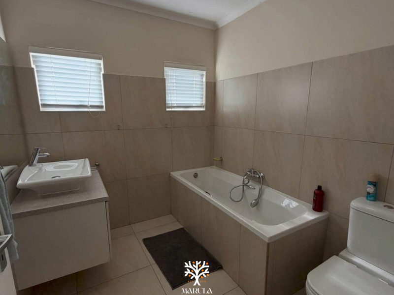 A functional bathroom featuring a built-in vanity with basin, a bathtub with handheld shower, and a toilet, finished with neutral wall and floor tiles.