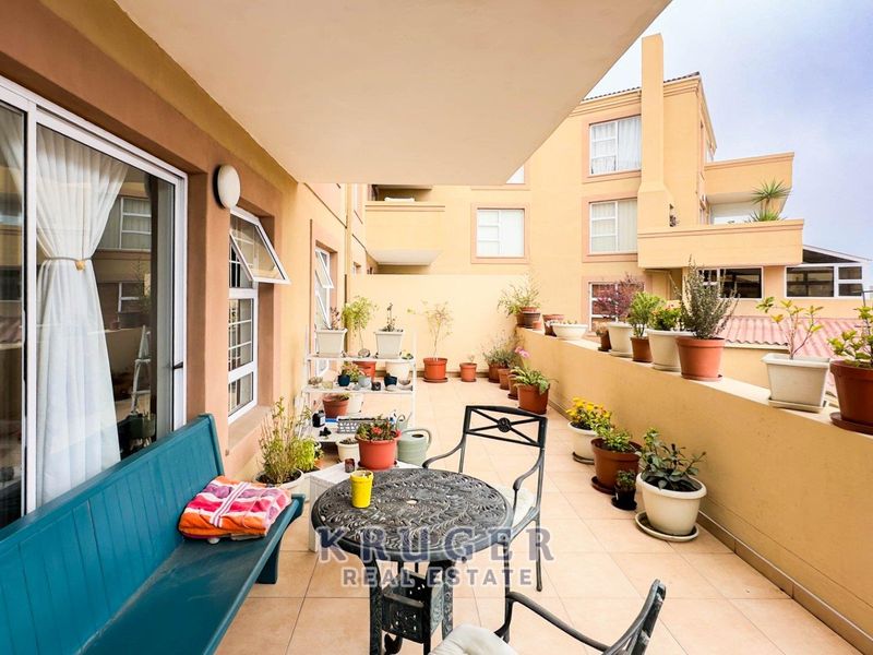 A spacious covered balcony featuring tiled flooring and a masonry balustrade, providing an outdoor extension to the apartment living area.
