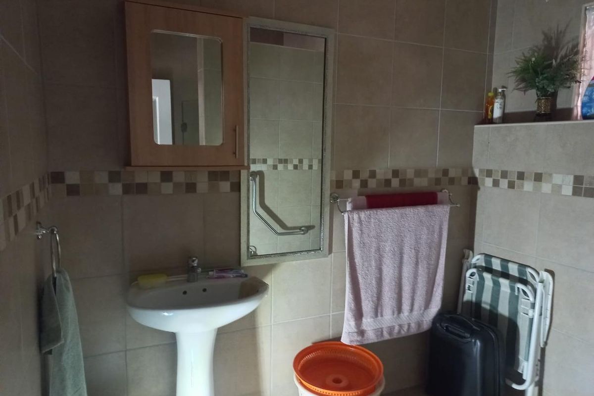 A functional bathroom featuring a pedestal basin, wall-mounted medicine cabinet, and neutral ceramic wall tiles with a decorative mosaic border.