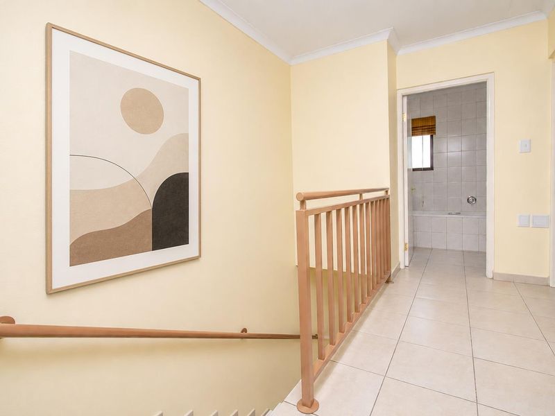 A bright upstairs hallway featuring tiled flooring and a staircase railing, leading towards a bathroom.