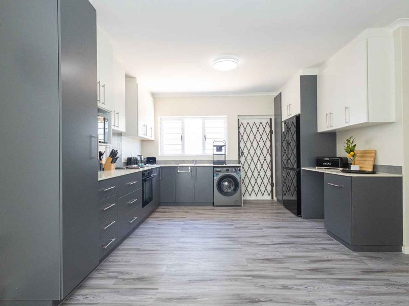 Modern kitchen featuring sleek grey and white cabinetry, laminate countertops, built-in oven, hob, and integrated laundry plumbing, finished with durable laminate flooring.