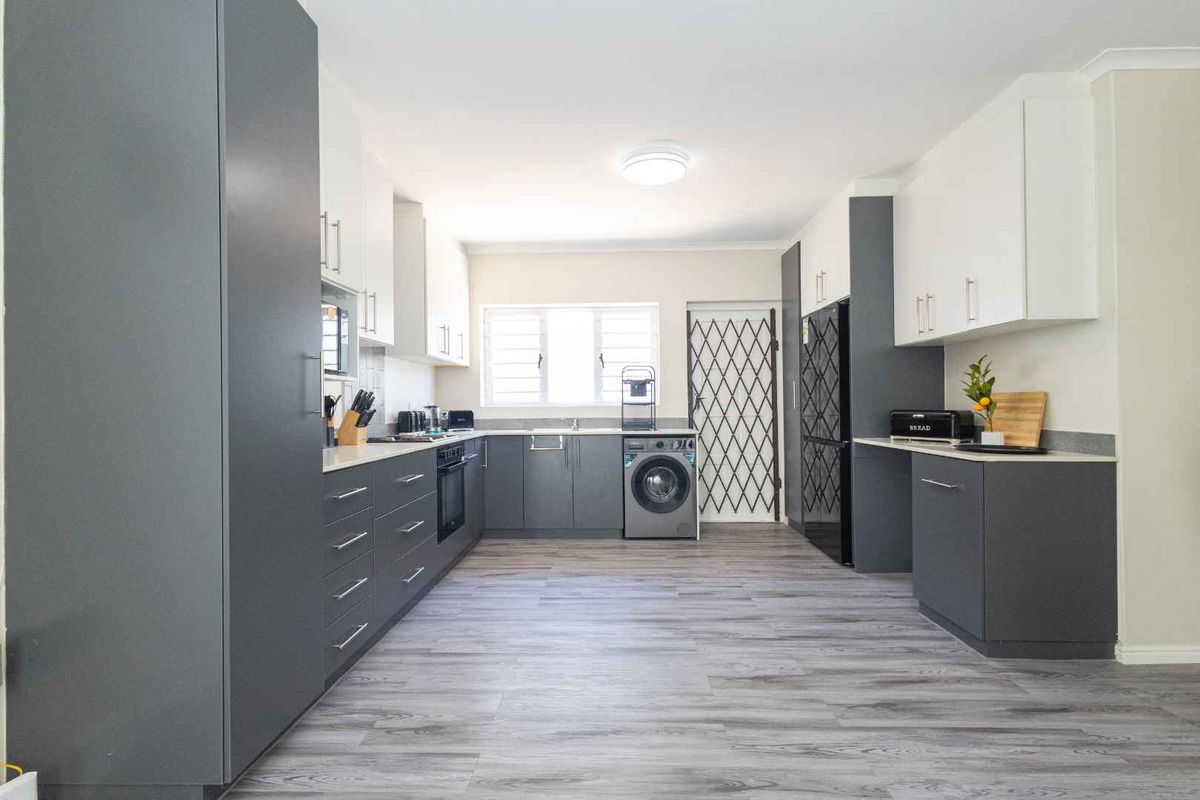 Modern kitchen featuring sleek grey and white cabinetry, laminate countertops, built-in oven, hob, and integrated laundry plumbing, finished with durable laminate flooring.
