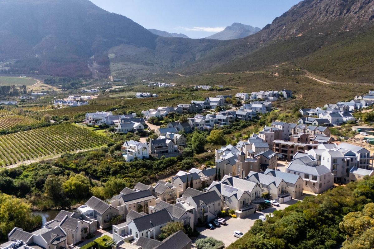Aerial view of a residential estate nestled in a valley, showcasing multiple apartment buildings, surrounding vineyards, and scenic mountain landscape.