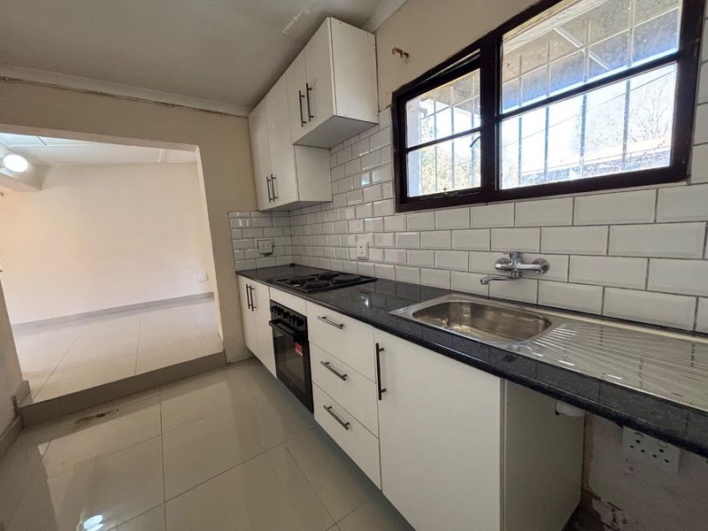 A functional kitchen featuring white cabinetry, granite countertops, a subway tile backsplash, and built-in cooking appliances, with an open-plan layout to the living area.