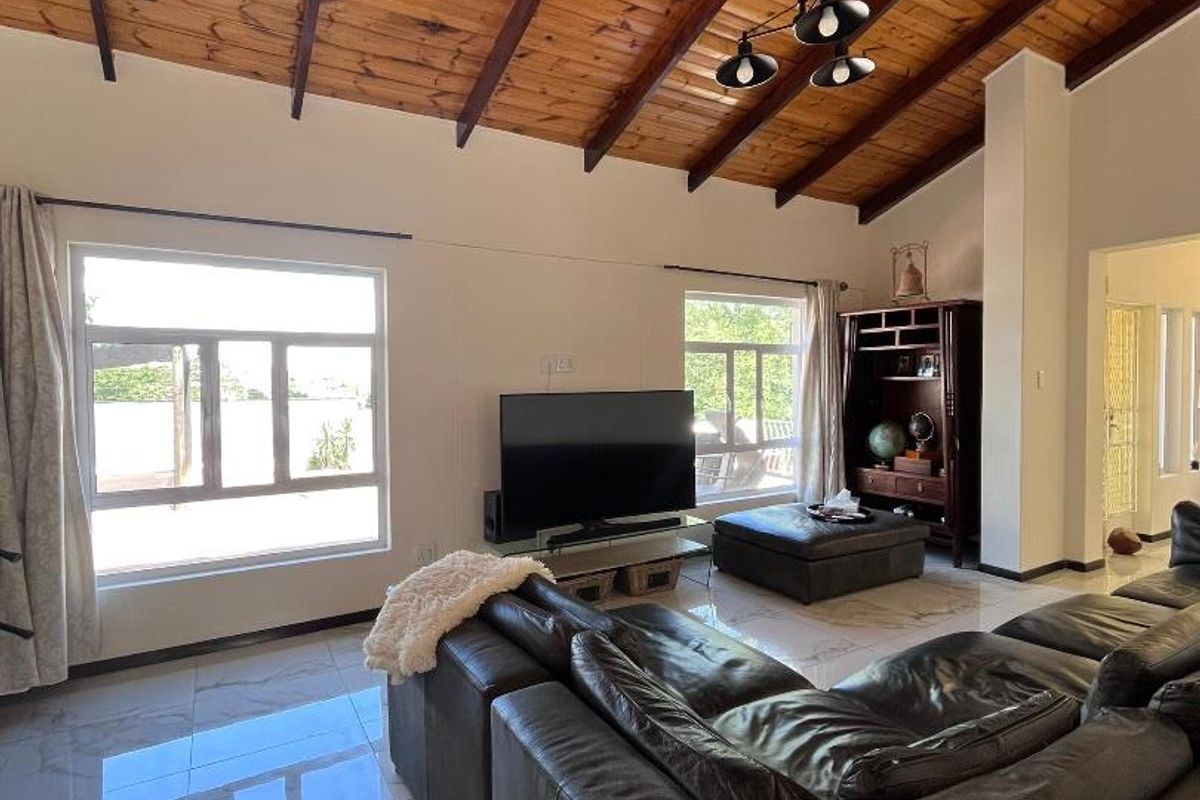Spacious living room featuring high vaulted timber-beamed ceilings, large windows for natural light, and polished marble-look floor tiles.