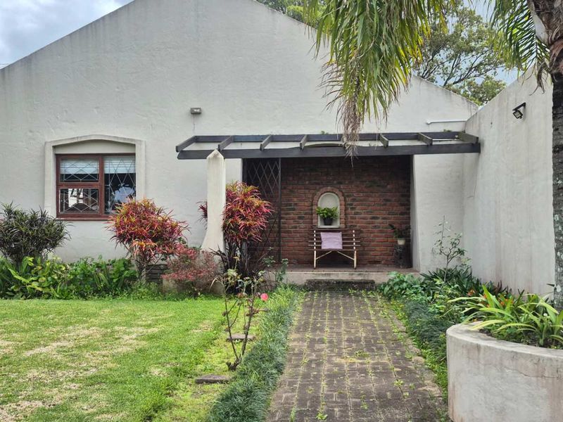 Rear exterior view featuring a brick facade, paved walkway, pergola, and established garden area with a concrete planter.