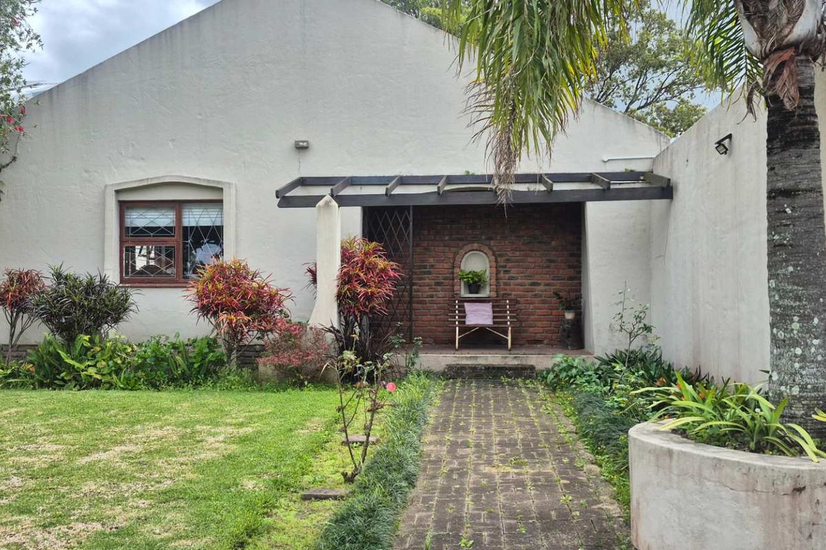Rear exterior view featuring a brick facade, paved walkway, pergola, and established garden area with a concrete planter.