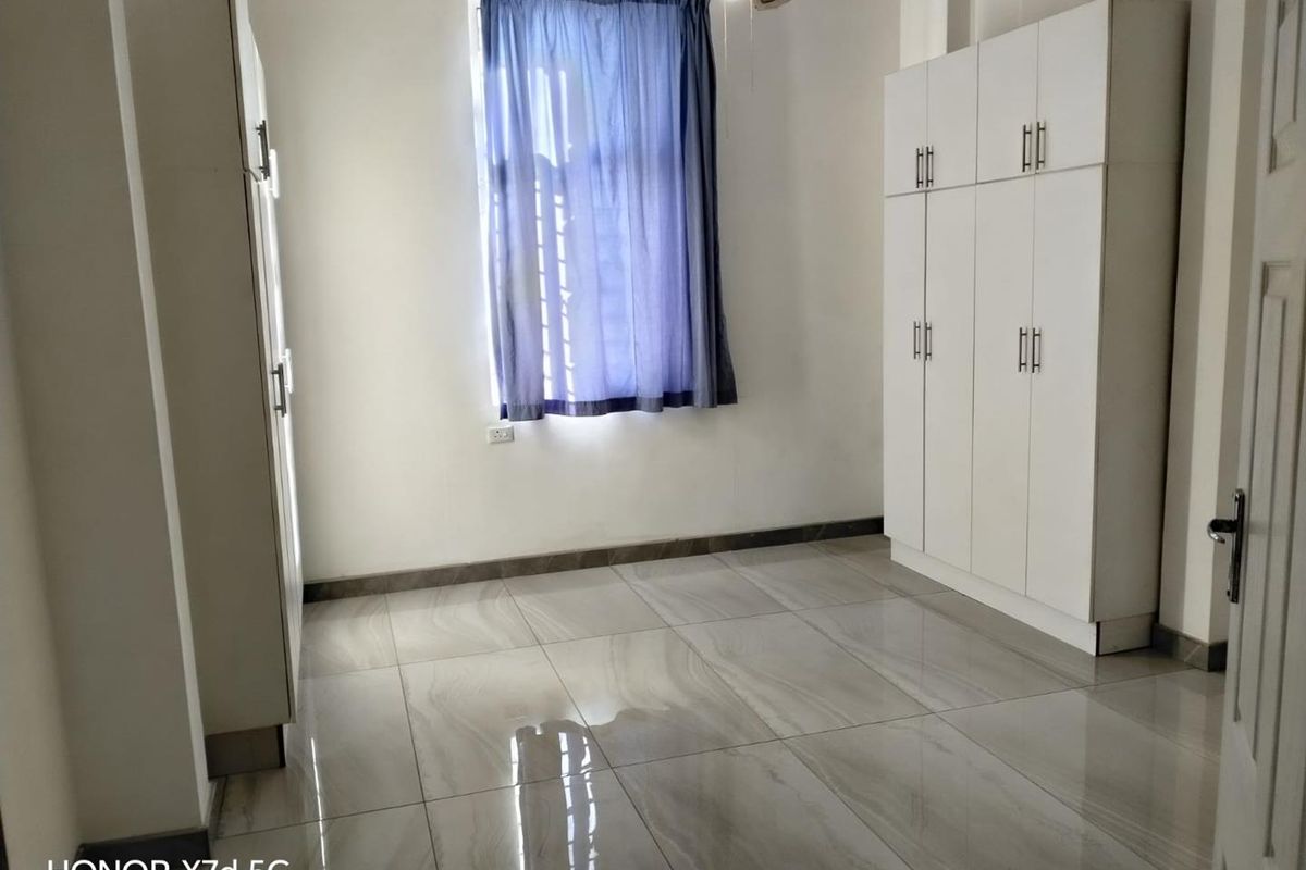 A bright, empty bedroom featuring modern tiled flooring and ample built-in cupboard storage space.