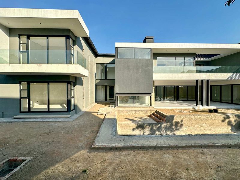 Modern double-story rear elevation featuring extensive glass sliding doors, balconies with glass balustrades, and an unfinished pool area awaiting landscaping.