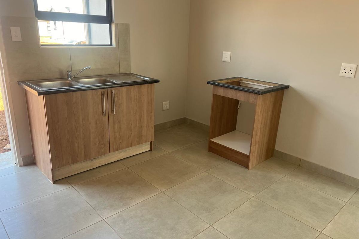 A compact kitchen area featuring tiled flooring, a double sink with laminate cabinetry, and an additional base unit with a countertop.