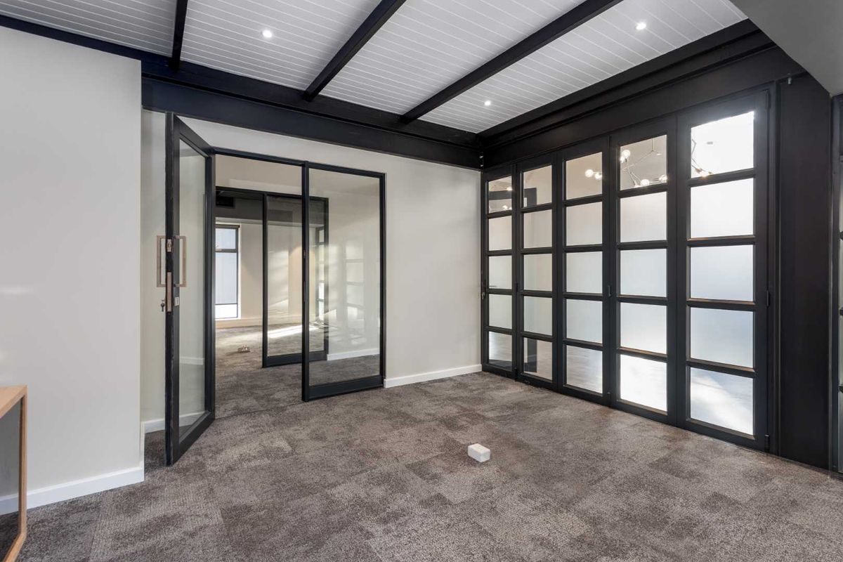 Modern office space featuring high-quality glass partitions, exposed ceiling beams, recessed lighting, and professional carpet flooring in a clean, open layout.