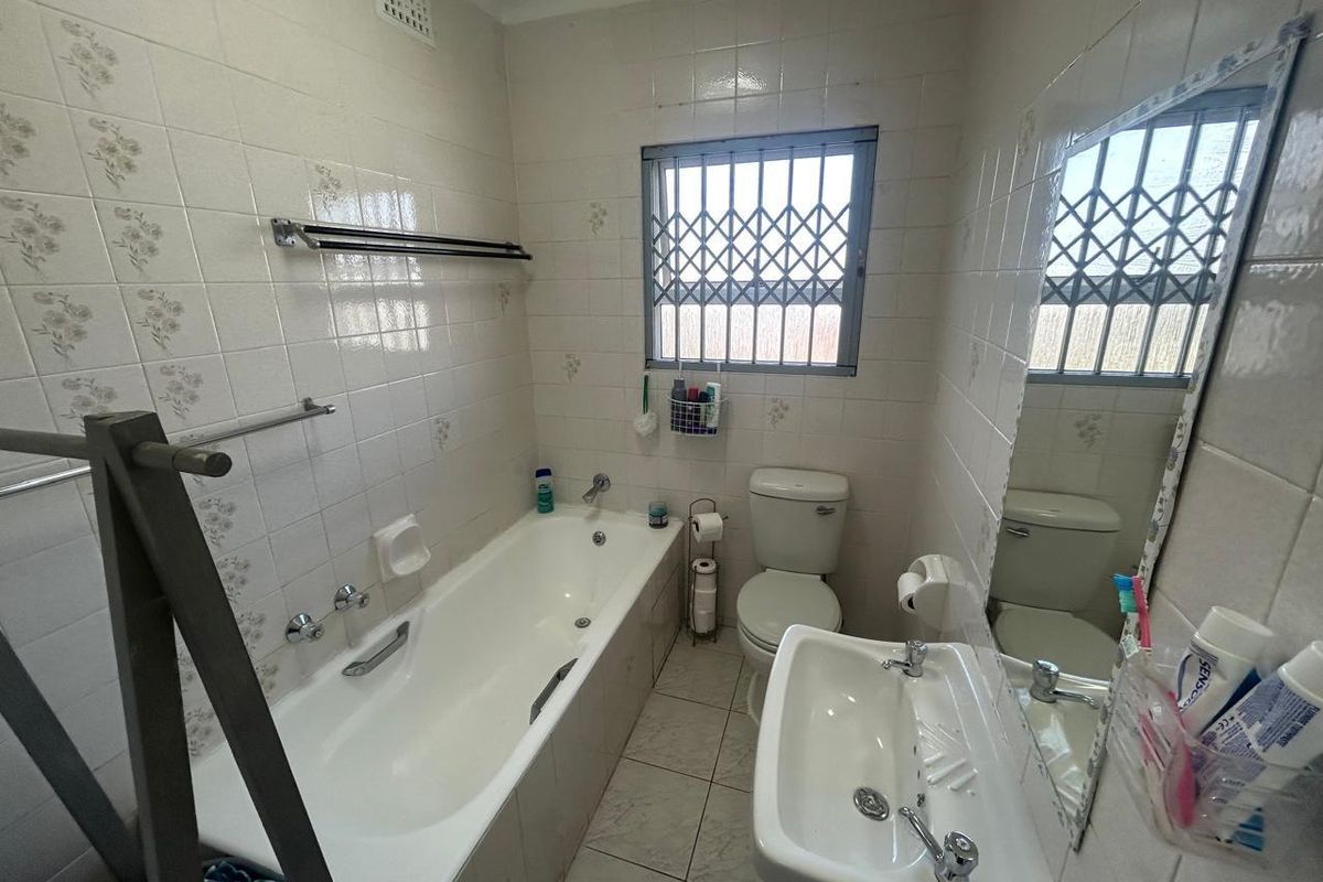 A functional bathroom featuring a built-in bathtub, wall-mounted basin, and toilet, finished with classic tiled walls and flooring.