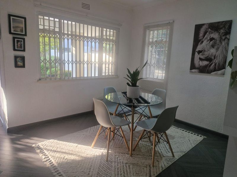A bright dining area featuring herringbone flooring, large windows with security gates, and venetian blinds, offering a clean and functional space.