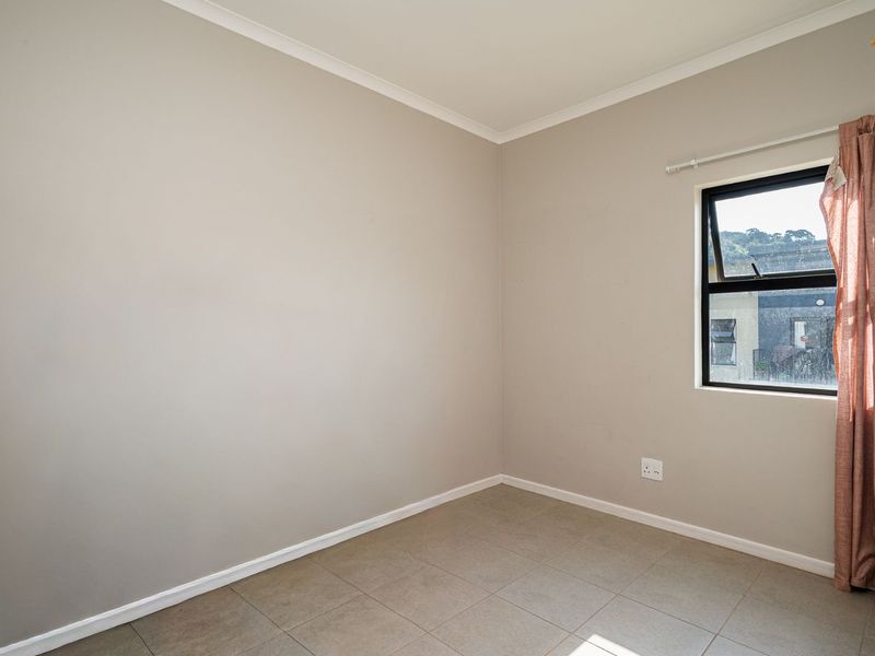 A clean, empty bedroom featuring neutral wall paint, tiled flooring, and an aluminium-framed window.