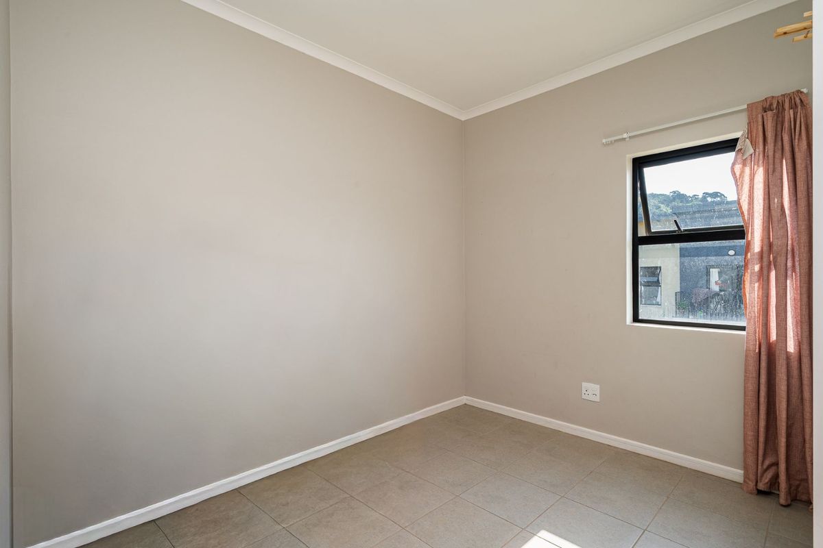 A clean, empty bedroom featuring neutral wall paint, tiled flooring, and an aluminium-framed window.
