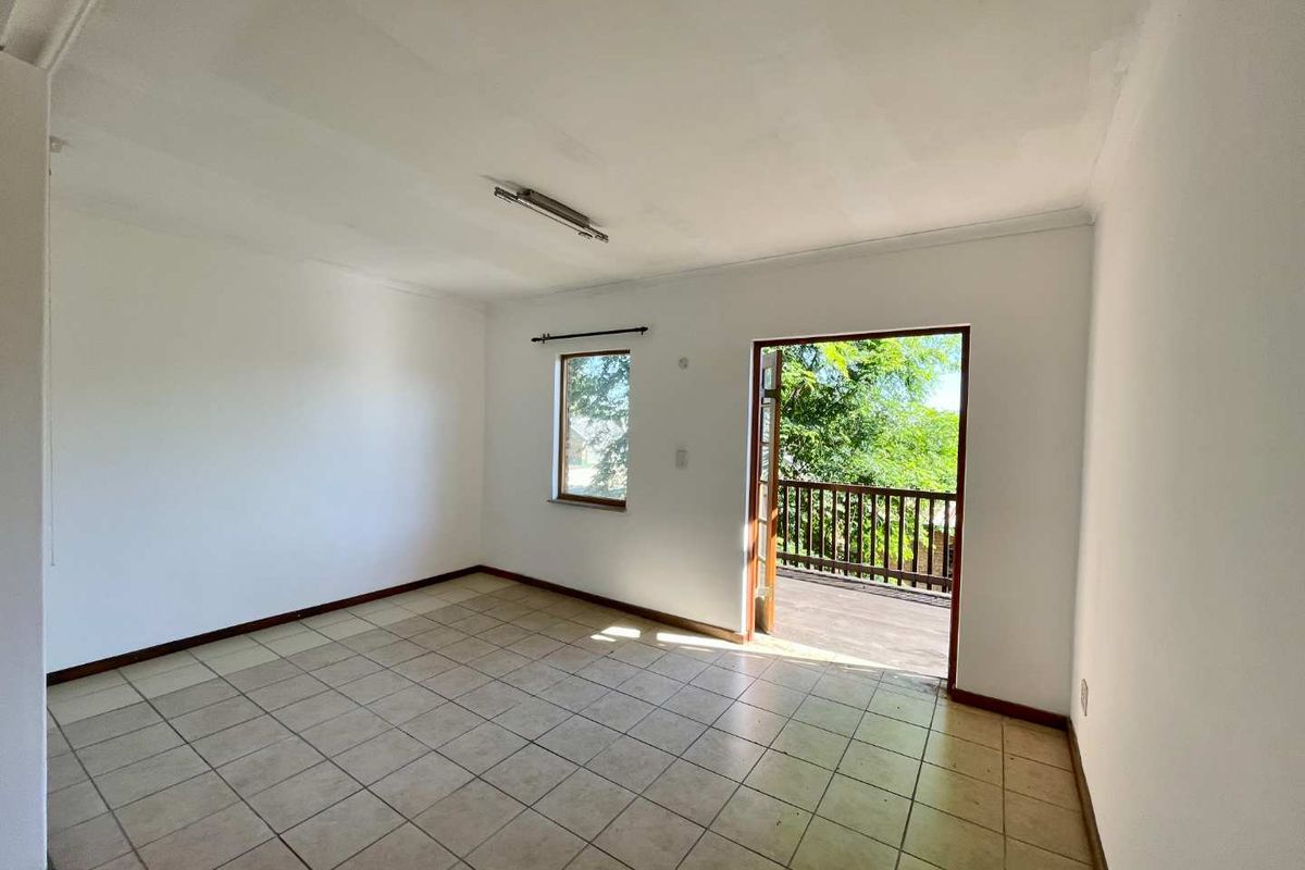 An empty bedroom featuring tiled flooring, a single window, and a door providing direct access to an outdoor balcony area.