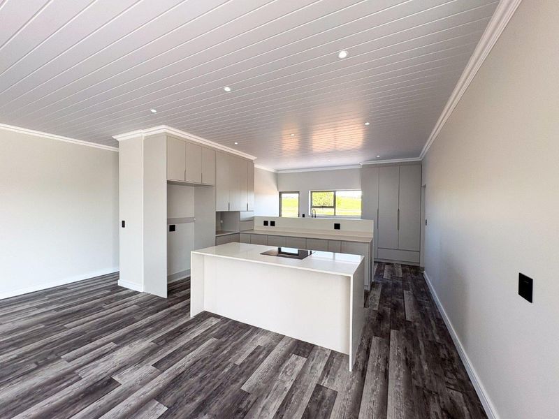 Modern, empty kitchen featuring a central island, sleek built-in cabinetry, recessed lighting, and wood-look laminate flooring in a clean, neutral space.