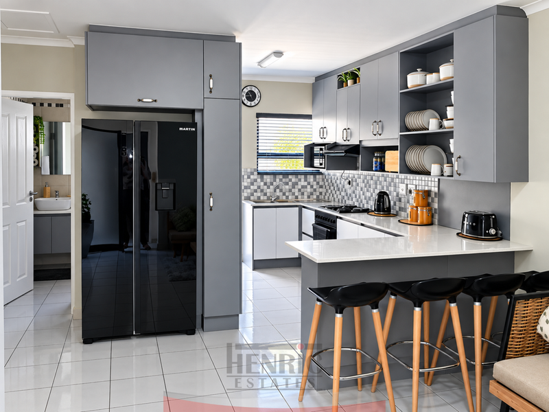 Modern kitchen featuring grey cabinetry, quartz countertops, a breakfast bar, tiled backsplash, and integrated appliances, with an adjacent view into a bathroom.