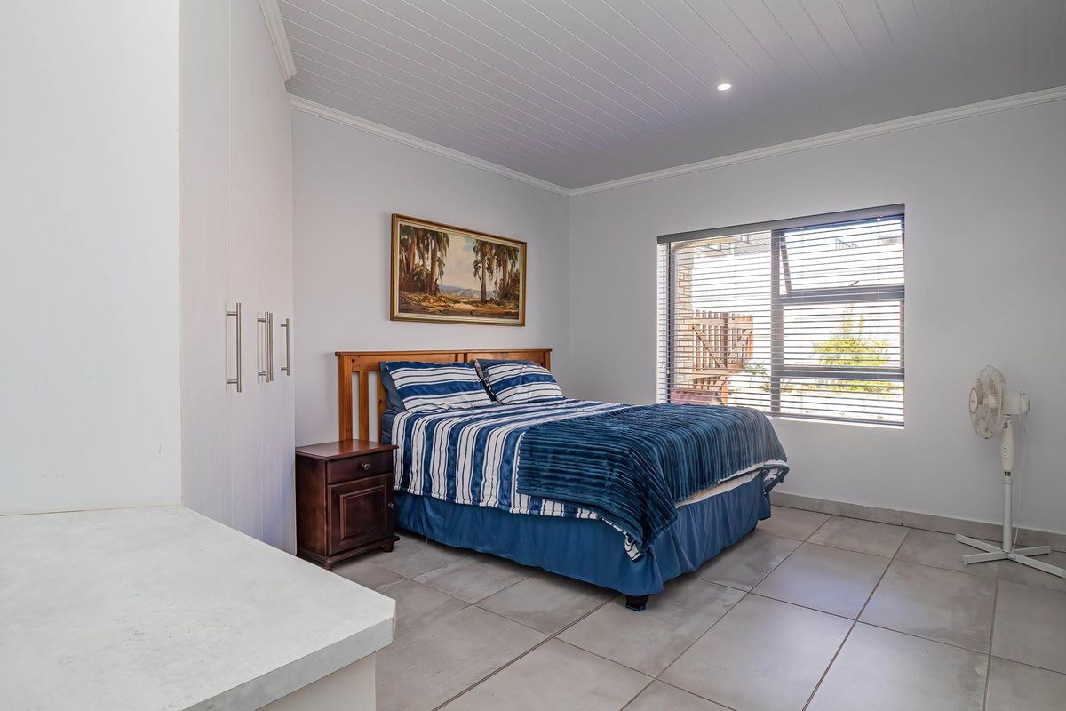 A well-maintained bedroom featuring neutral tiled flooring, built-in cupboards, and a classic tongue and groove ceiling with natural light from the window.