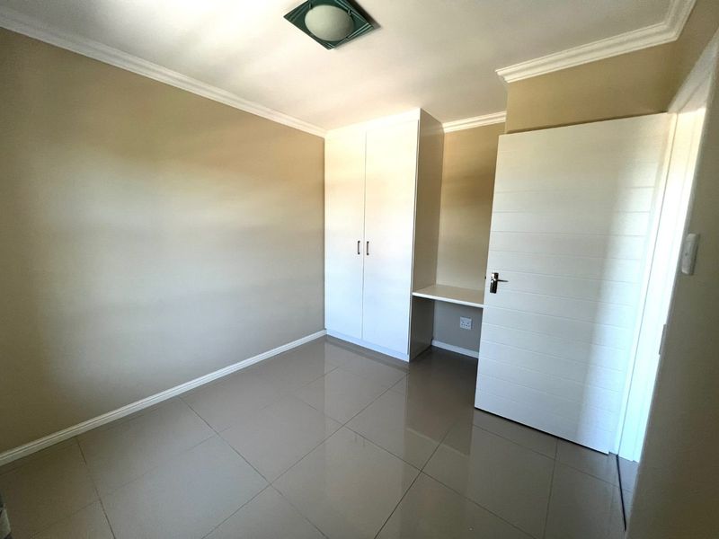 A clean, empty bedroom featuring neutral tiled flooring, built-in cupboards, and a convenient integrated desk space.