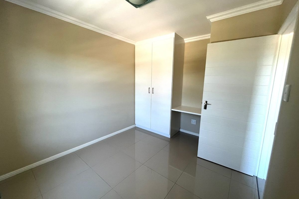 A clean, empty bedroom featuring neutral tiled flooring, built-in cupboards, and a convenient integrated desk space.