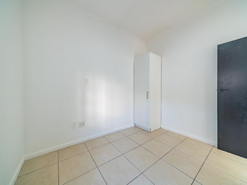 A clean, empty bedroom featuring neutral tiled flooring and a built-in cupboard, providing a versatile space ready for personalization.