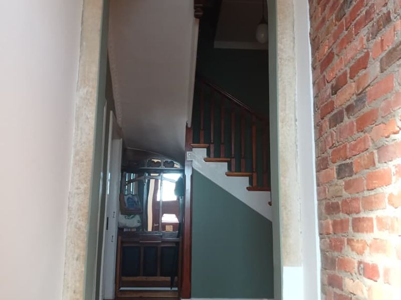 A characterful hallway featuring an arched entryway, exposed brickwork, and a timber staircase, showcasing classic architectural details and hardwood flooring.