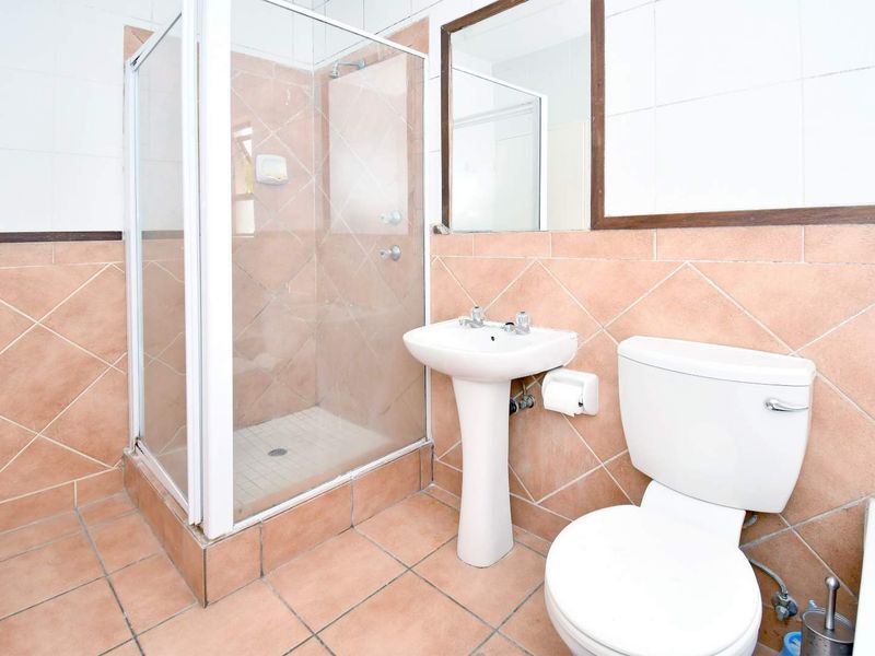 A functional bathroom featuring a shower enclosure, pedestal basin, and toilet with dated wall and floor tiling.
