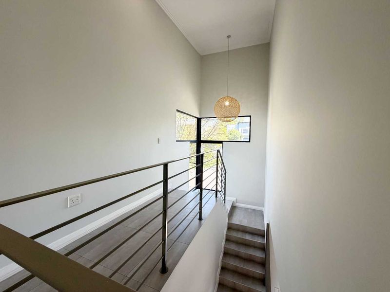 A bright and modern hallway featuring a sleek metal balustrade, tiled staircase, and large windows that provide ample natural light.