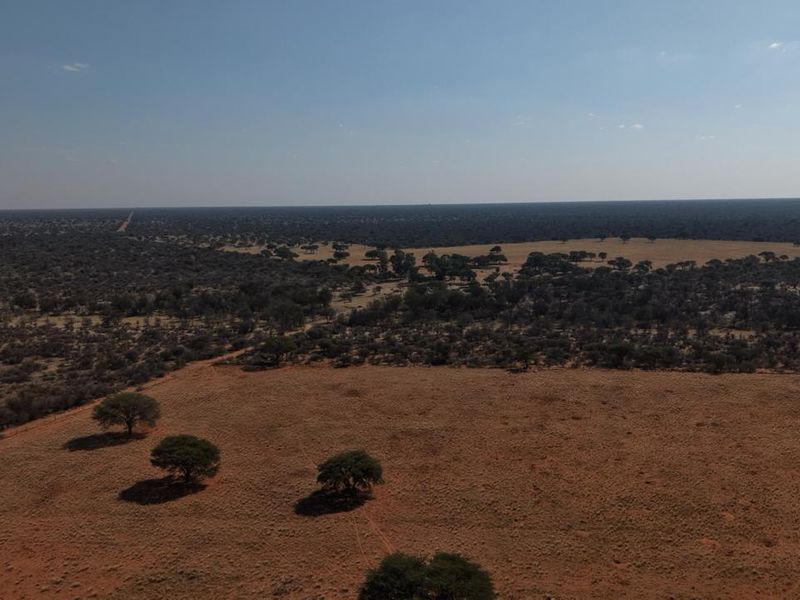 An expansive aerial view of the farm property, showcasing vast open grazing land, native trees, and the surrounding rural landscape.
