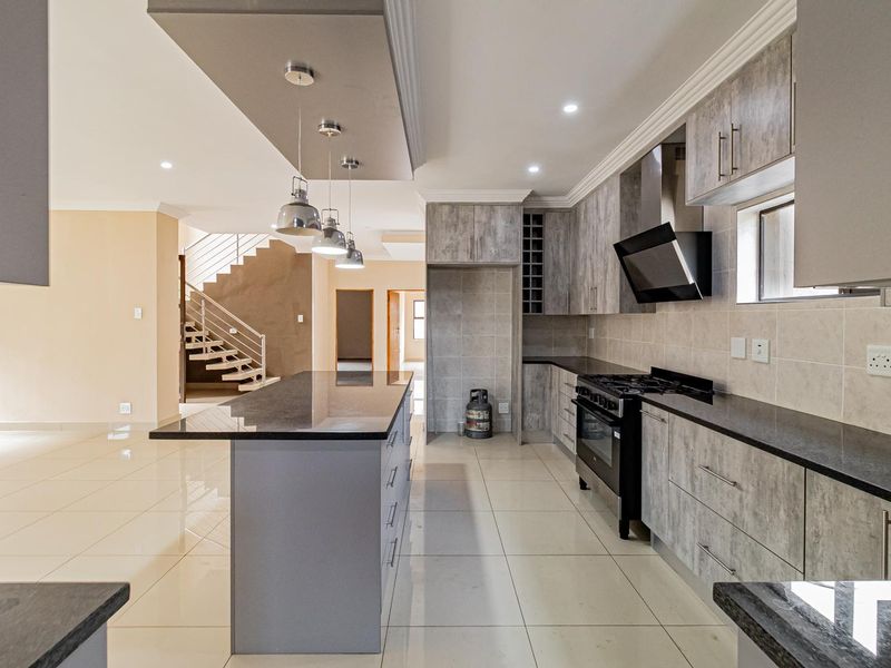 Modern open-plan kitchen featuring a central island, granite countertops, built-in cabinetry, and a gas stove, seamlessly flowing into the living area.