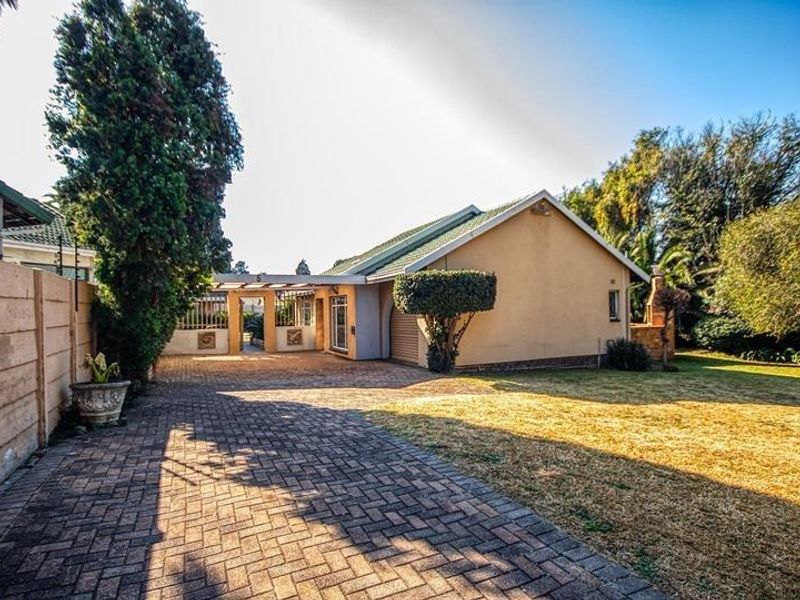 Front view of the property featuring a paved driveway, carport, and established garden with boundary wall and electric fencing.
