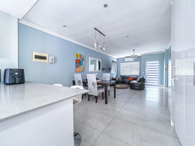 Spacious open-plan living and dining area featuring modern porcelain floor tiles, recessed lighting, and a sleek kitchen breakfast bar.