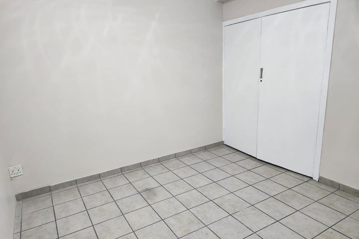 An empty bedroom featuring neutral tiled flooring and a built-in cupboard, providing a blank canvas for personalization.