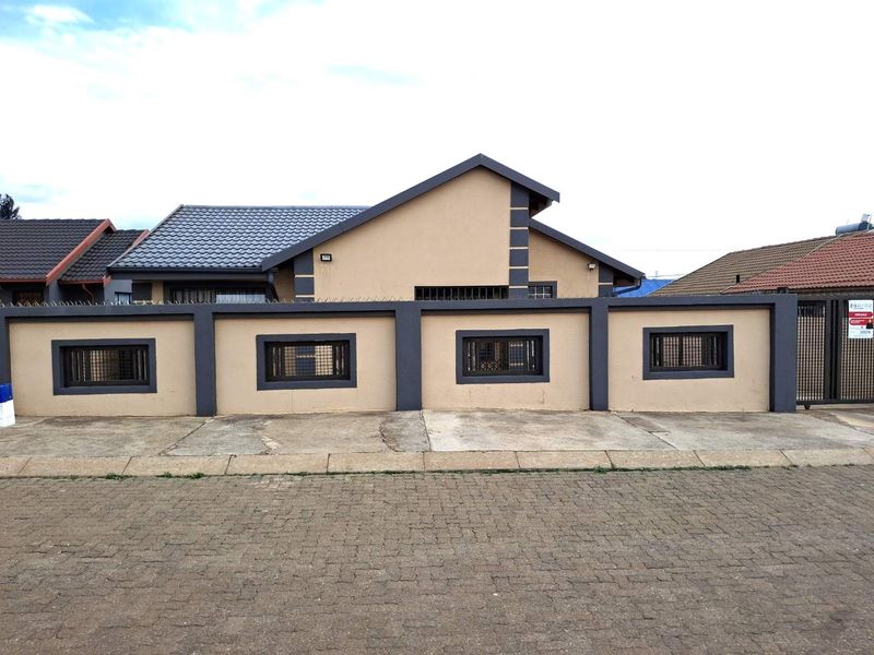Front view of a residential house featuring a secure perimeter wall with spikes, a tiled roof, and a paved driveway.