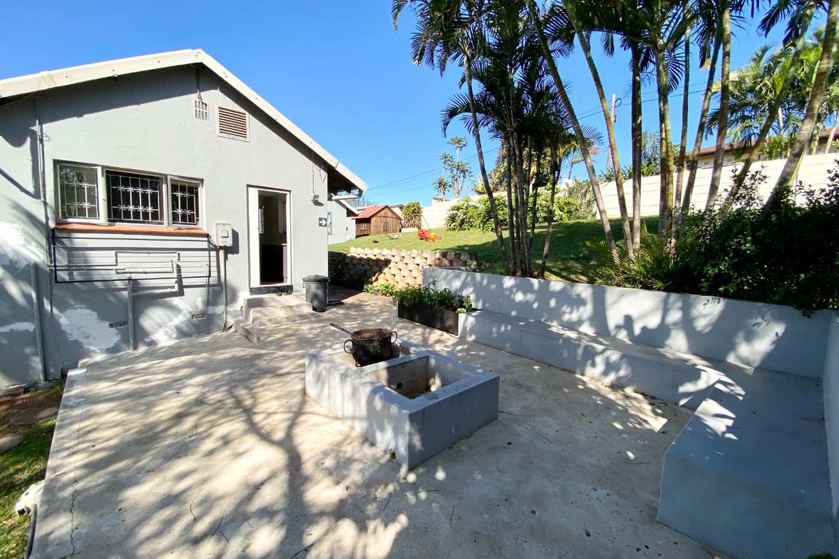 A rear patio area featuring a built-in concrete fire pit and bench seating, set against a landscaped garden with mature palm trees.