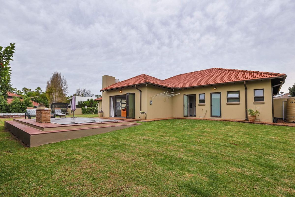 Rear view of the house featuring a raised deck with a swimming pool cover, landscaped lawn, and multiple access points to the interior.