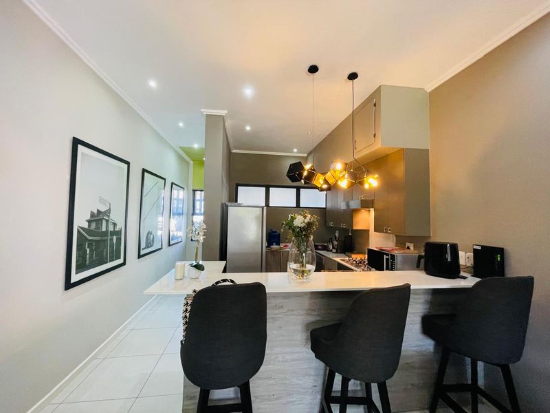 Modern open-plan kitchen featuring a breakfast bar, sleek cabinetry, stone countertops, and contemporary pendant lighting, seamlessly integrated with the living area.
