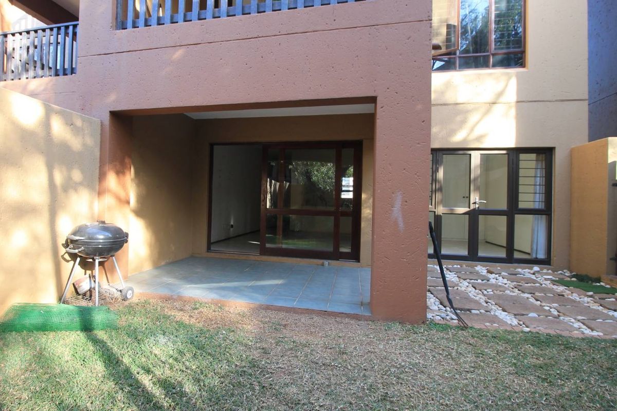 Rear view of the apartment featuring a covered patio with tiled flooring, sliding glass doors, and a small garden area with stone paving.