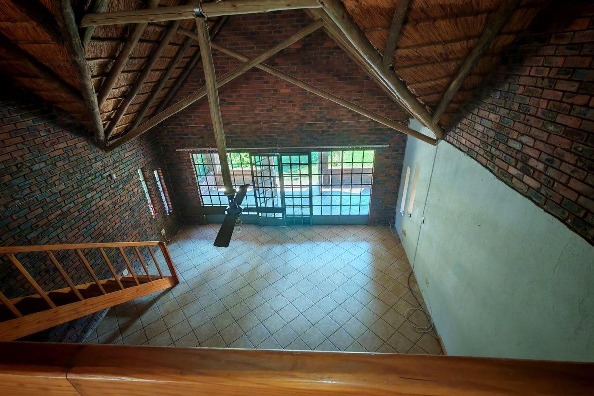 Spacious double-volume living area featuring exposed brick walls, a traditional thatched roof, tiled flooring, and large glass sliding doors leading to the patio.