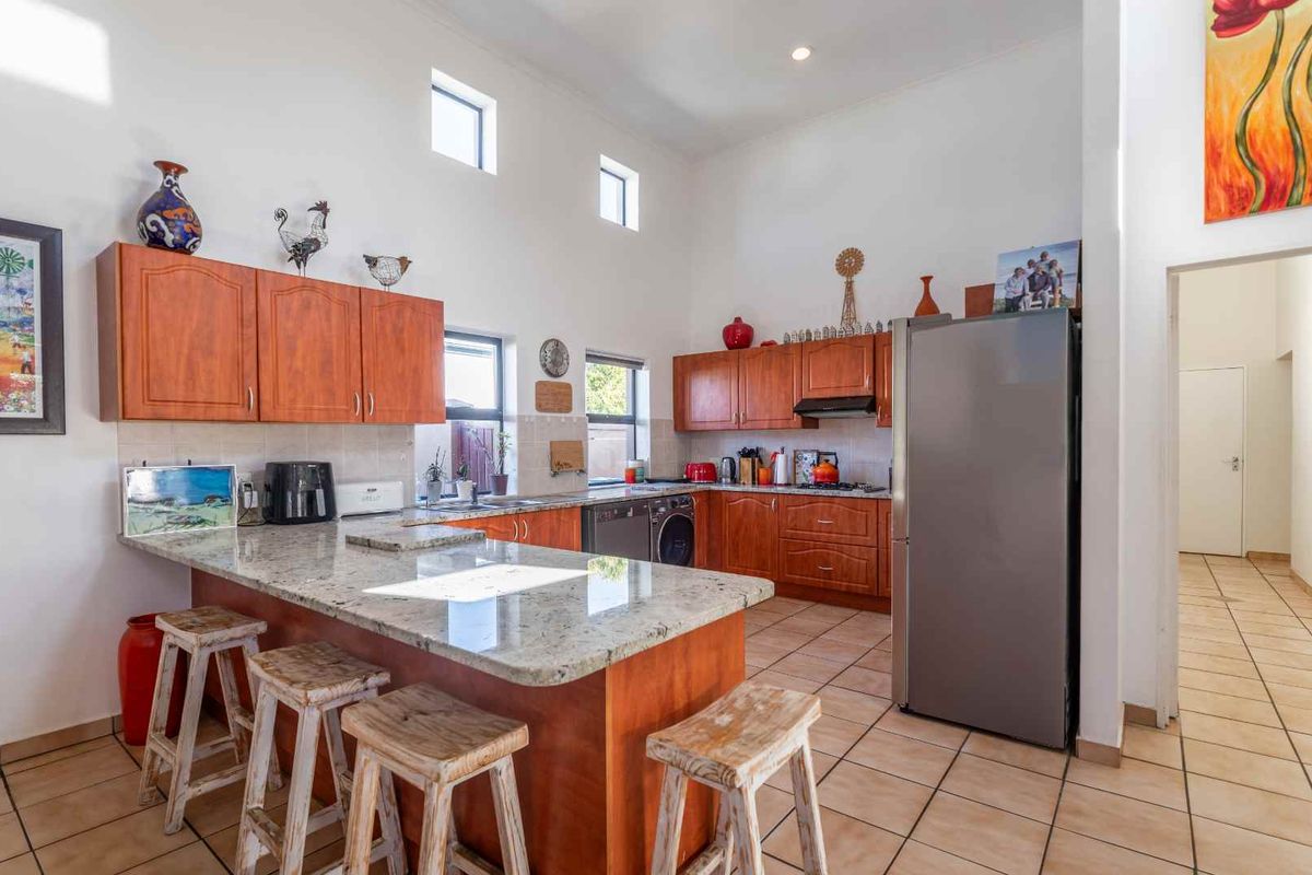 Spacious kitchen featuring wooden cabinetry, granite countertops, a breakfast bar, and tiled flooring with high ceilings and natural light.