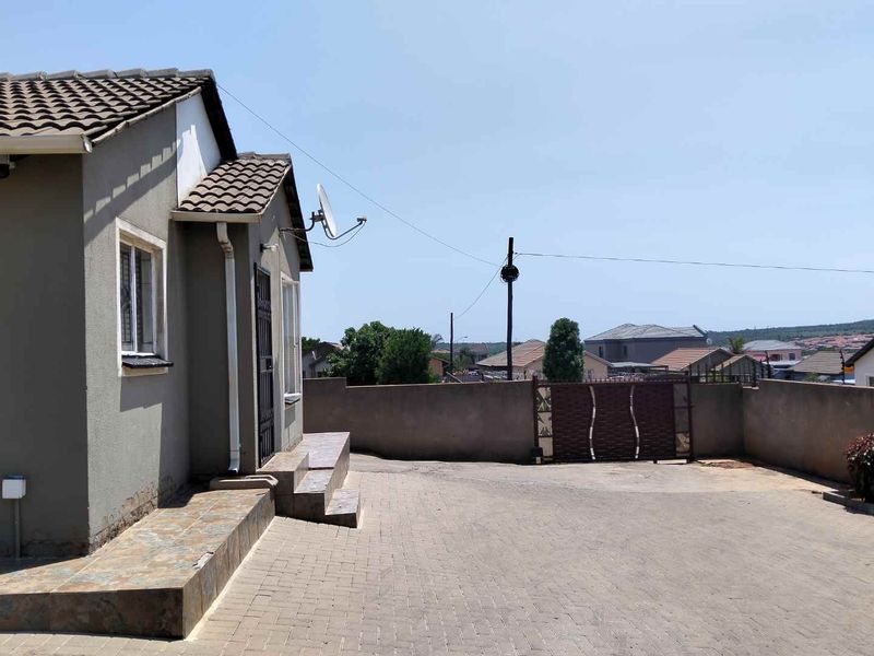 Front exterior view of the property featuring a paved driveway, boundary wall with metal gate, and tiled entrance steps.