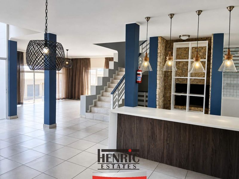 Spacious open-plan living area featuring a stone accent wall, built-in shelving, a modern kitchen island, and a central staircase with tiled flooring throughout.