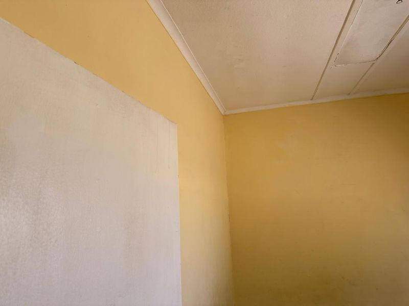 A corner view of an interior room showing yellow painted walls, ceiling coving, and a ceiling access panel with visible surface wear.