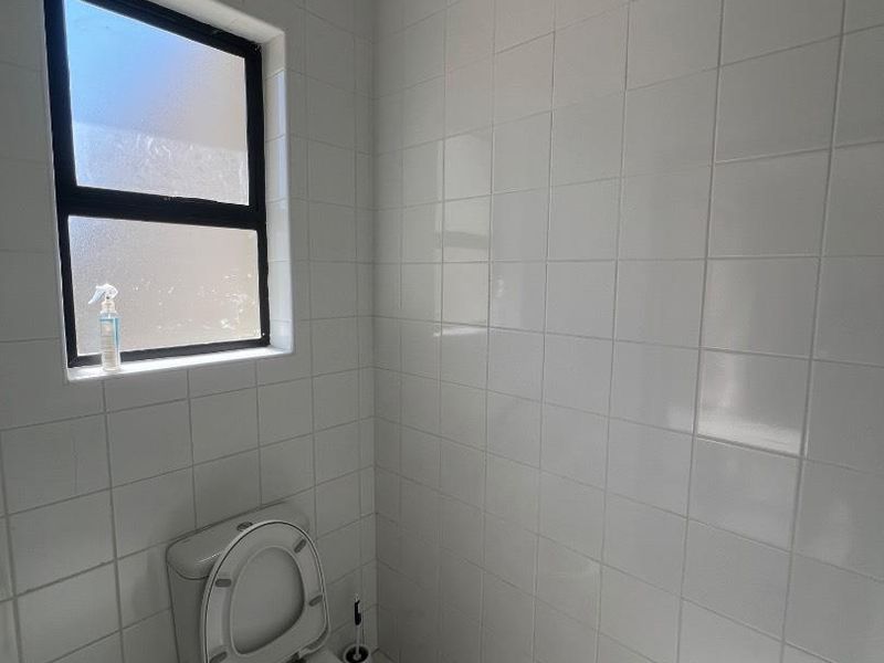 A compact bathroom featuring white wall tiles, tiled flooring, and a frosted glass window for privacy.