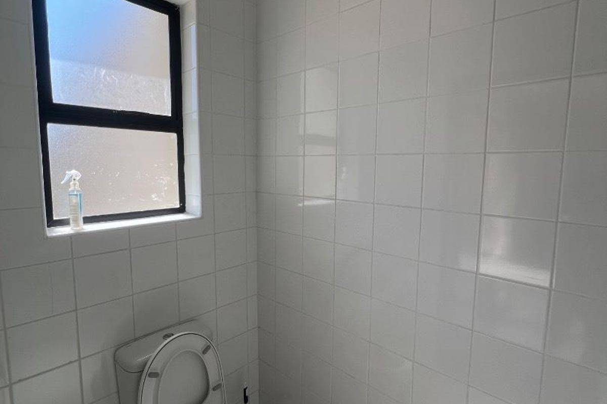 A compact bathroom featuring white wall tiles, tiled flooring, and a frosted glass window for privacy.