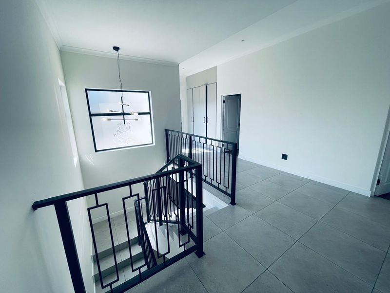 A bright and modern upper-level landing featuring tiled flooring, a sleek metal balustrade, and built-in storage cupboards.