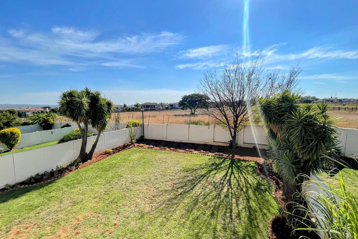 A private rear garden featuring a manicured lawn, established trees, and perimeter boundary walls, offering an open outlook over the surrounding landscape.