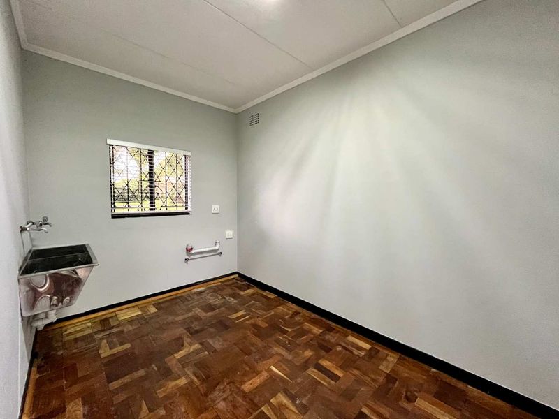 A functional laundry room featuring parquet flooring, a stainless steel utility sink, and plumbing connections for laundry appliances.