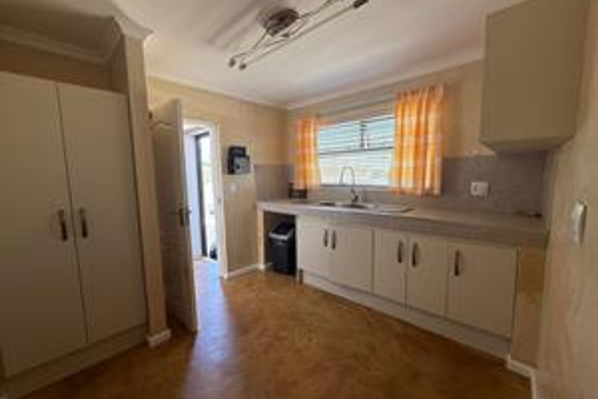 A functional kitchen featuring built-in cabinetry, laminate countertops, and a stainless steel sink, with direct access to an exterior door.